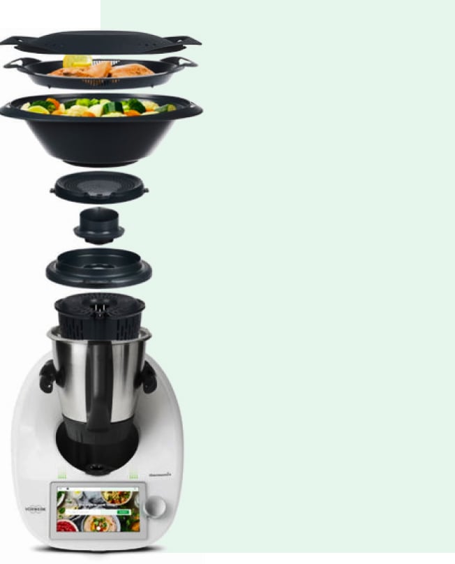 Thermomix with the bowl, lid, steaming basket, Varoma layers all floating above it, showing you how layered cooking works