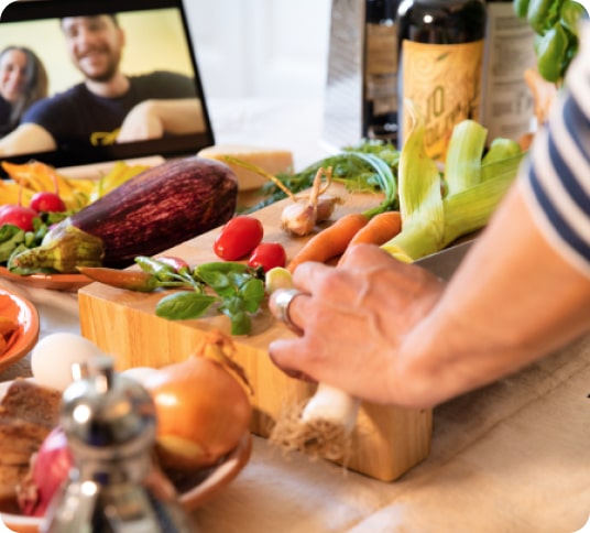 hand holding a chopping knife by a chopping board with lot's of colourful veggies. Person is watching a cooking demonstration on an mobile phone